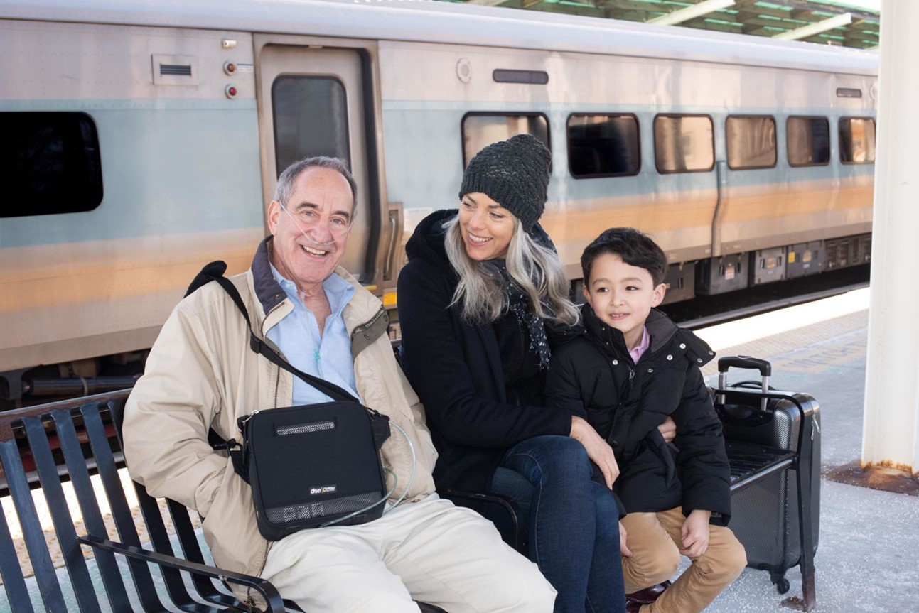 A family sitting on a bench in front of a train

Description automatically generated